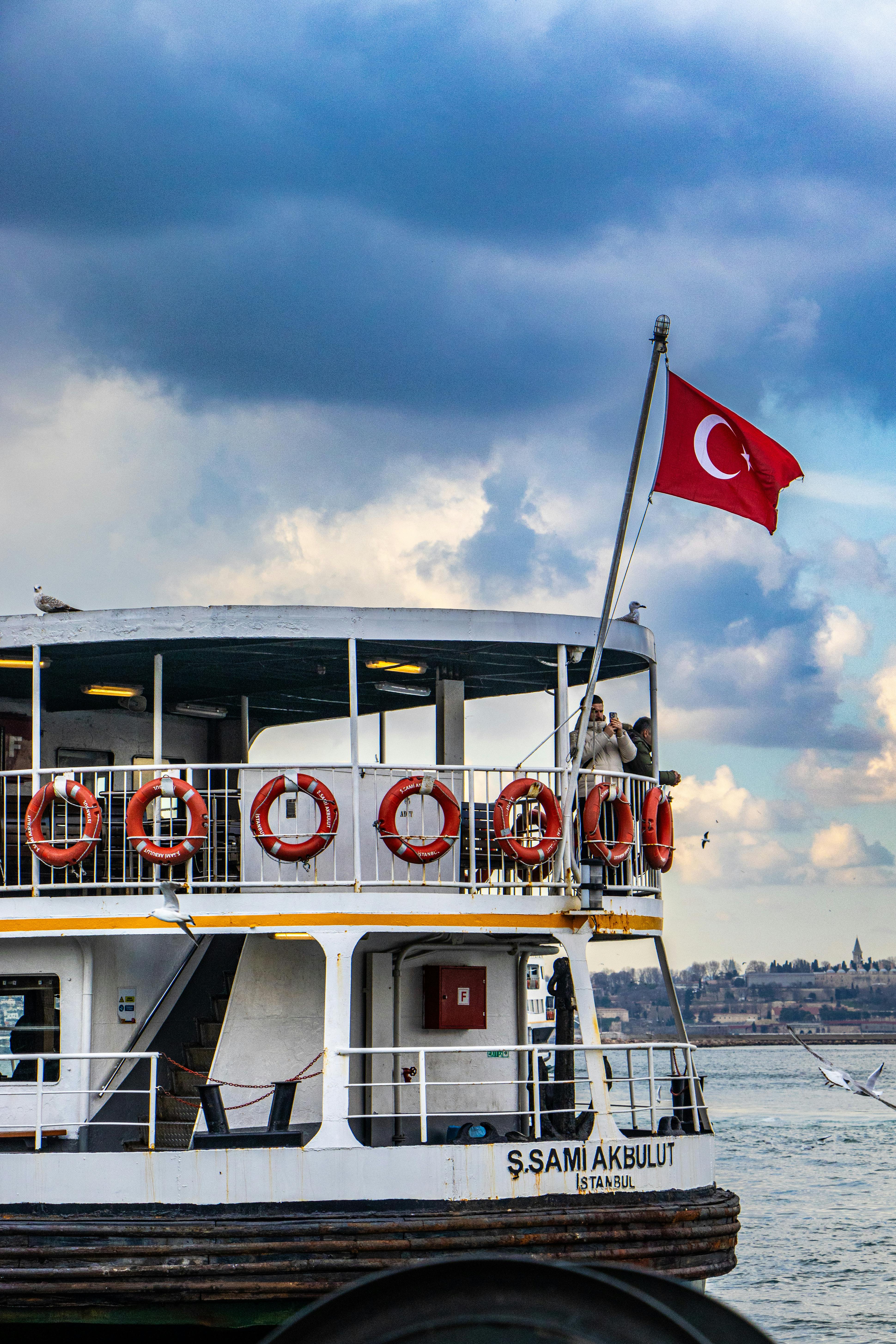 Ferry with Turkish flag cruising in Istanbul, showcasing vibrant clouds and skyline.