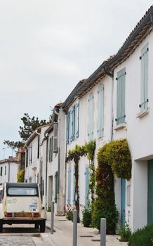 A scenic view of a quaint French village street featuring traditional houses and a vintage car parked along the roadside.