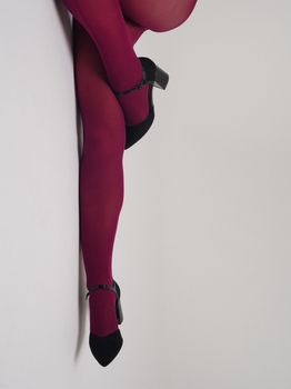 Stylish legs wearing burgundy stockings and black heels against a plain background.