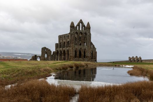 Whitby Abbey ruins reflected in a pond during winter in Whitby, UK.