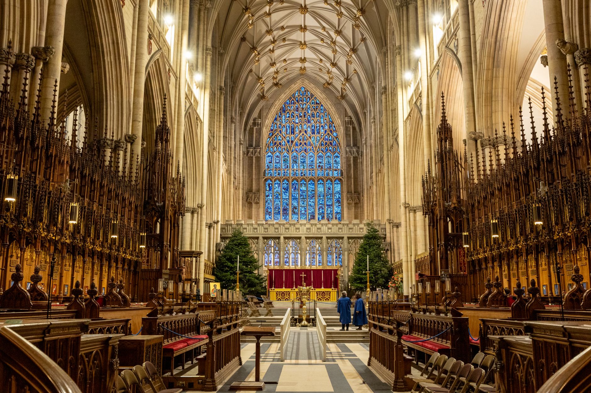 Gothic interior of York Minster with clergy present, decorated for Christmas with trees and illuminated stained glass windows.