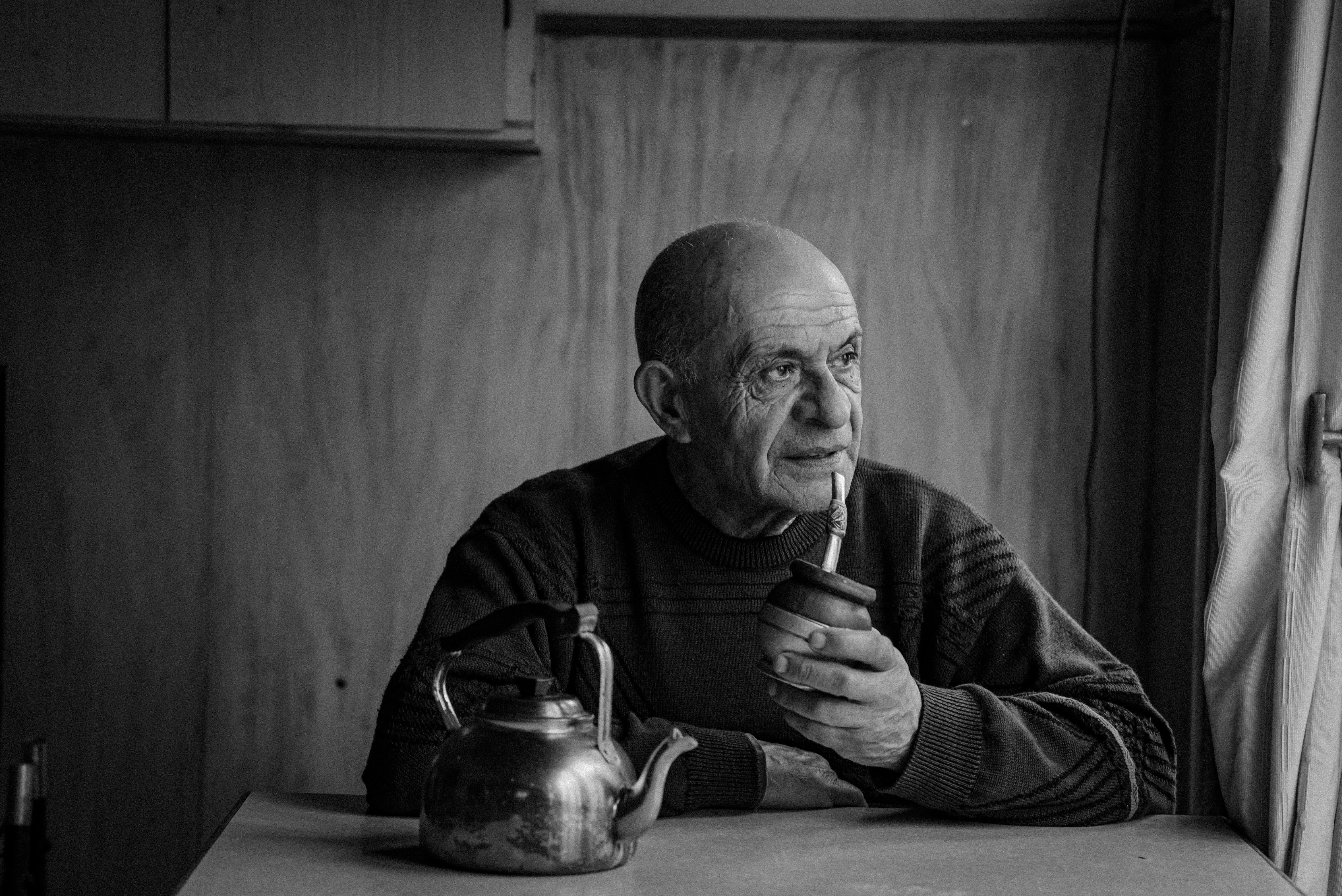 Black and white portrait of an elderly man enjoying mate indoors, reflecting mood.