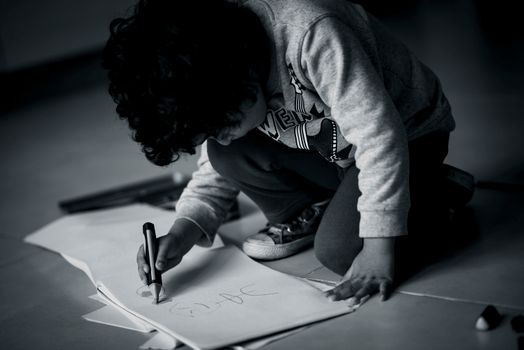 A young child intently drawing with a marker on paper indoors, captured in black and white.