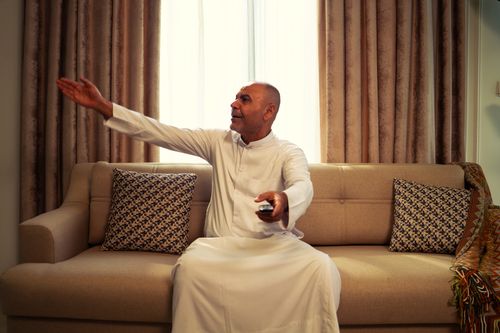 Free Senior man in traditional attire gesturing while watching TV at home, enjoying leisure time. Stock Photo