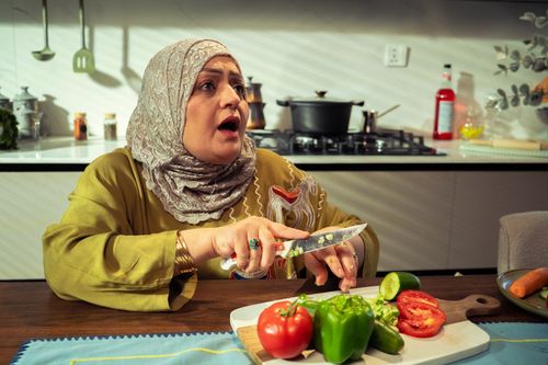 Free Middle Eastern woman preparing vegetables in modern kitchen, expressing surprise. Stock Photo