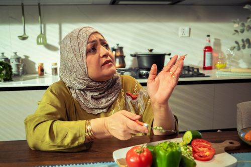 Free Middle-Eastern woman in hijab chopping vegetables in a modern kitchen with natural light. Stock Photo