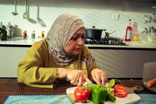 Free A middle-aged woman in a kitchen chopping fresh vegetables with care. Stock Photo