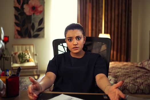 A woman seated at a home desk expressing confusion or concern, with a cozy room backdrop.