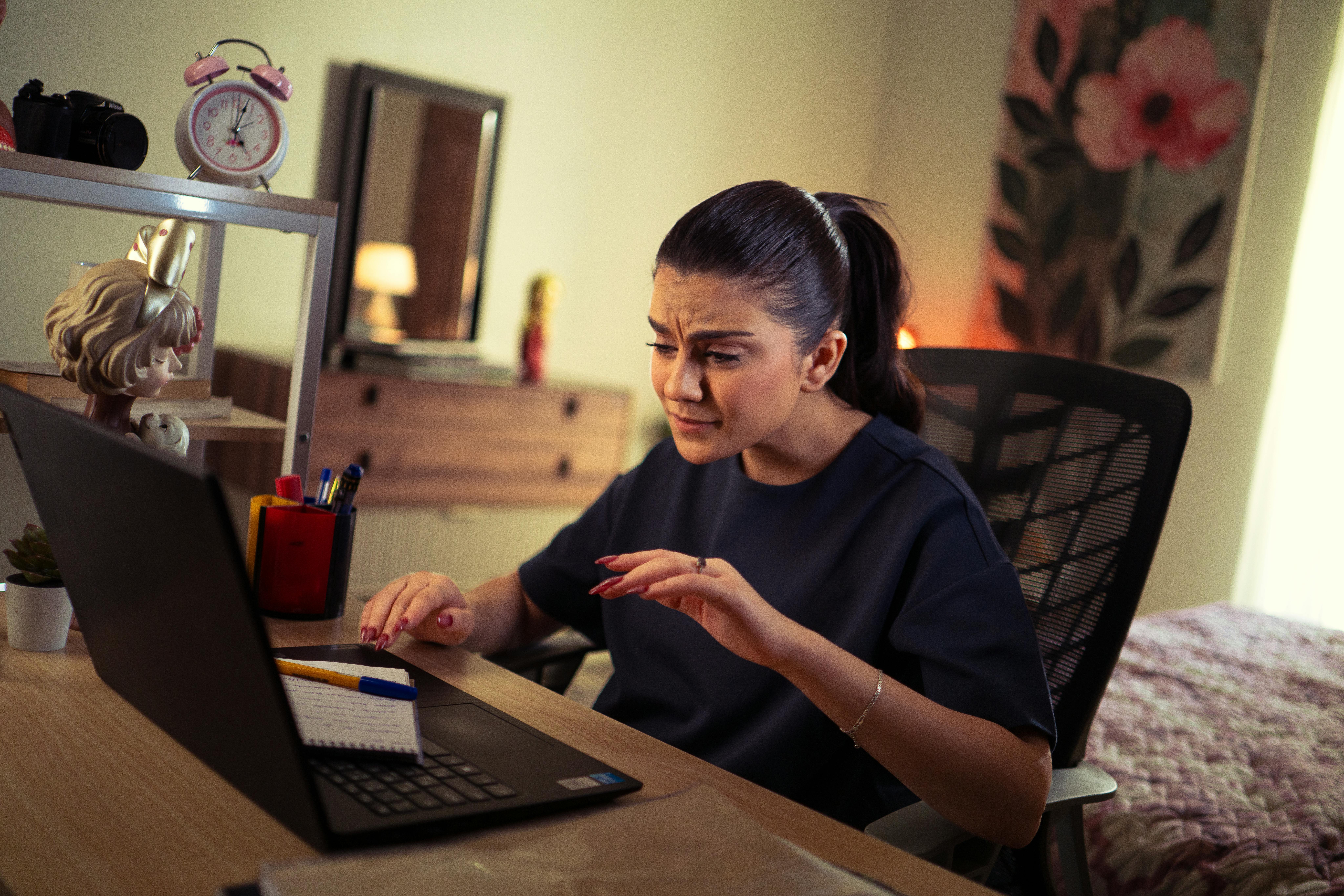 Woman concentrating on laptop work at home desk with office supplies.