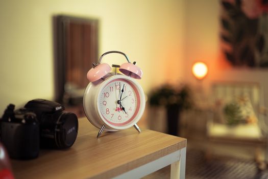 A pink vintage alarm clock on a wooden table with a cozy room background, perfect for nostalgia-themed decor.