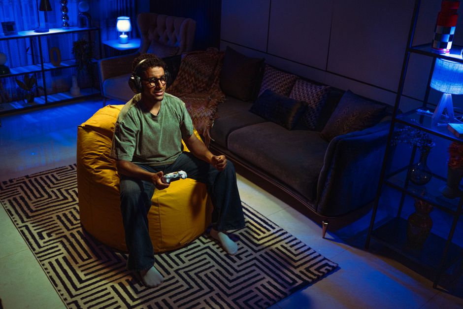 A man enjoying video games on a bean bag in a dimly lit living room with modern decor.