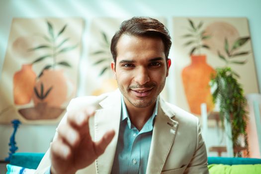 Confident businessman reaching towards camera in modern casual office setting.