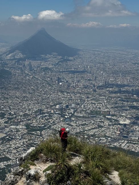 Hiker overlooks sprawling cityscape of Monterrey with Cerro de la Silla in distance.
