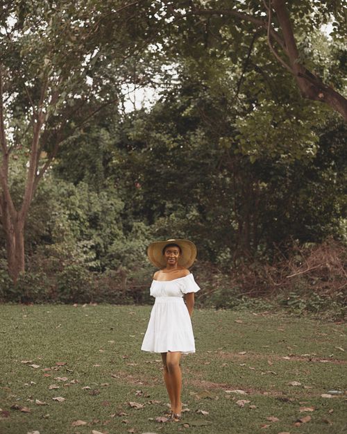 Free A woman wearing a white dress and hat stands in a serene forest clearing. Stock Photo