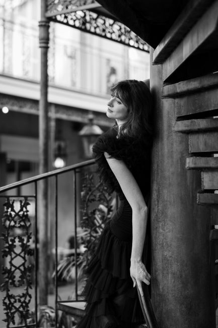 Elegant black and white portrait of a woman in a stylish dress leaning on a column.
