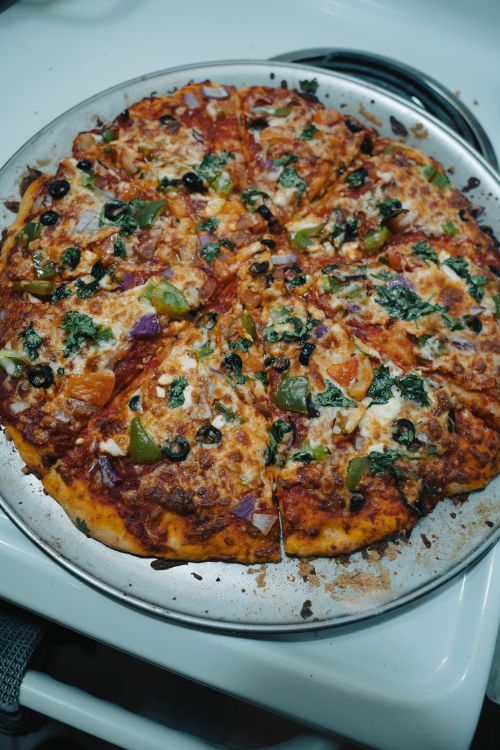 Free Delicious homemade vegetable pizza with olives, peppers, and cheese on a metal tray in an indoor lighting setting. Stock Photo