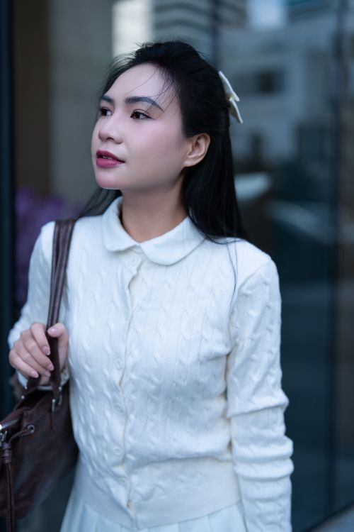 Free Elegant woman outdoors wearing a white sweater, looking away thoughtfully. Stock Photo
