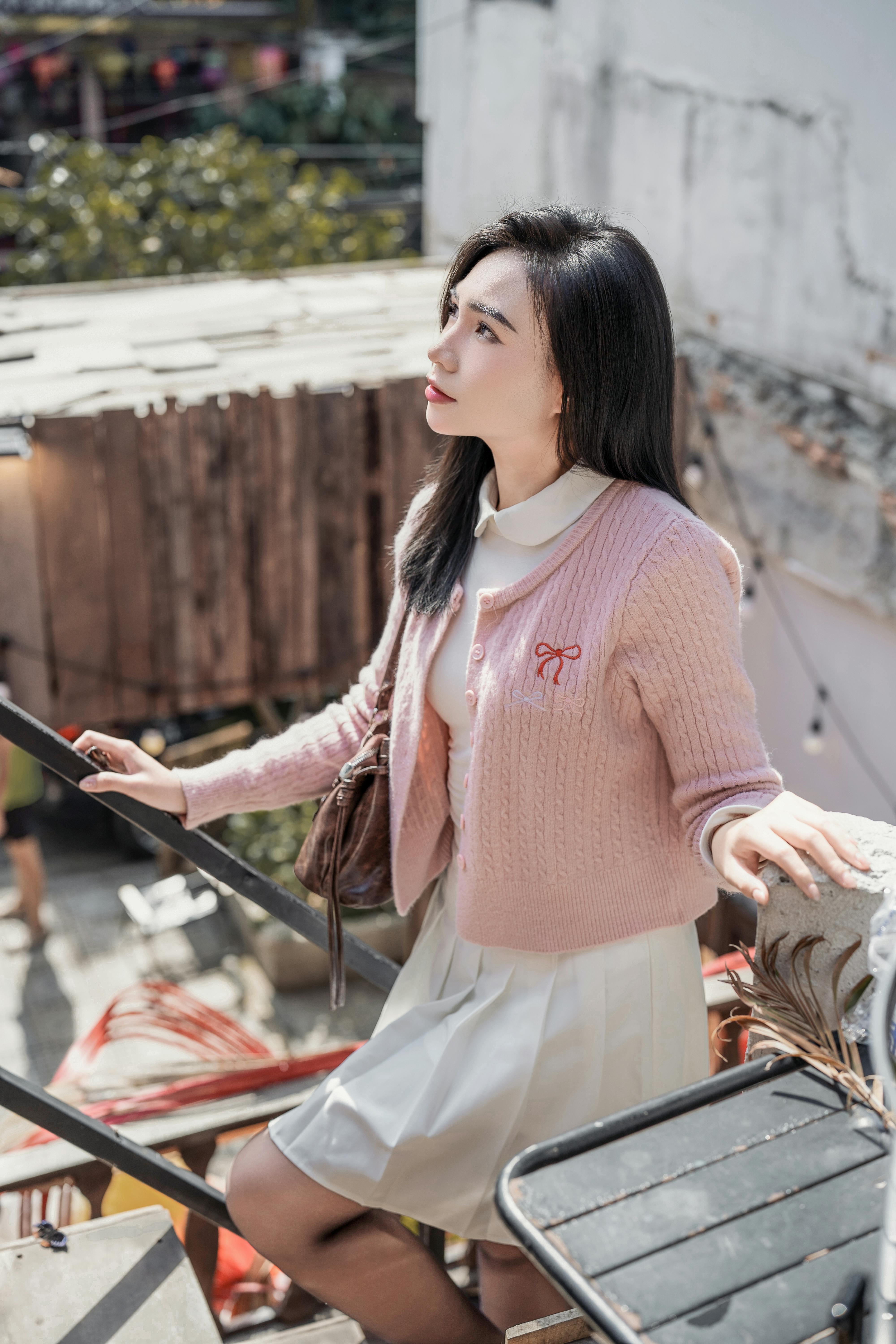 Stylish woman in pastel outfit posing on rustic staircase outdoors.