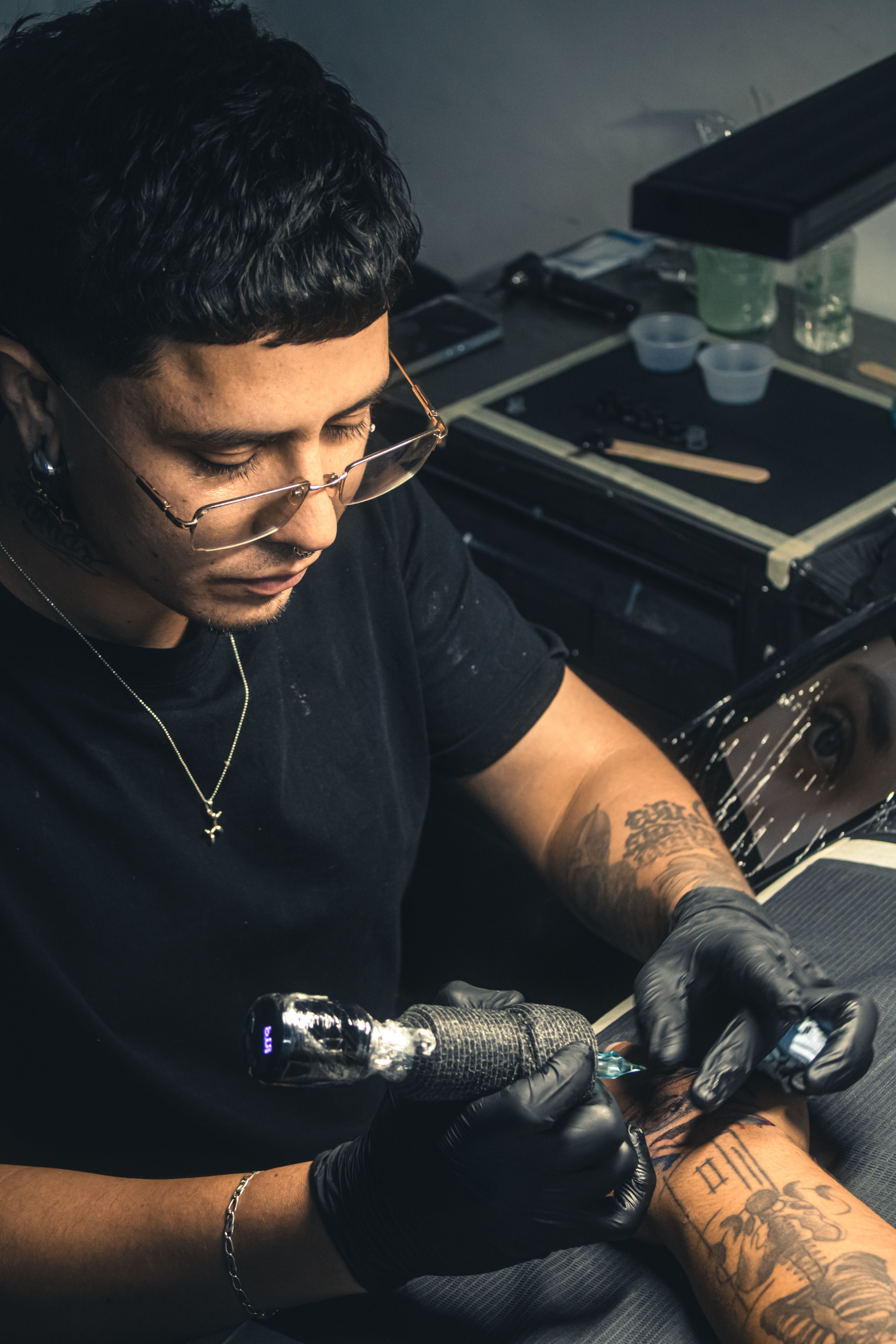 A professional tattoo artist creating an intricate arm tattoo in a studio setting.