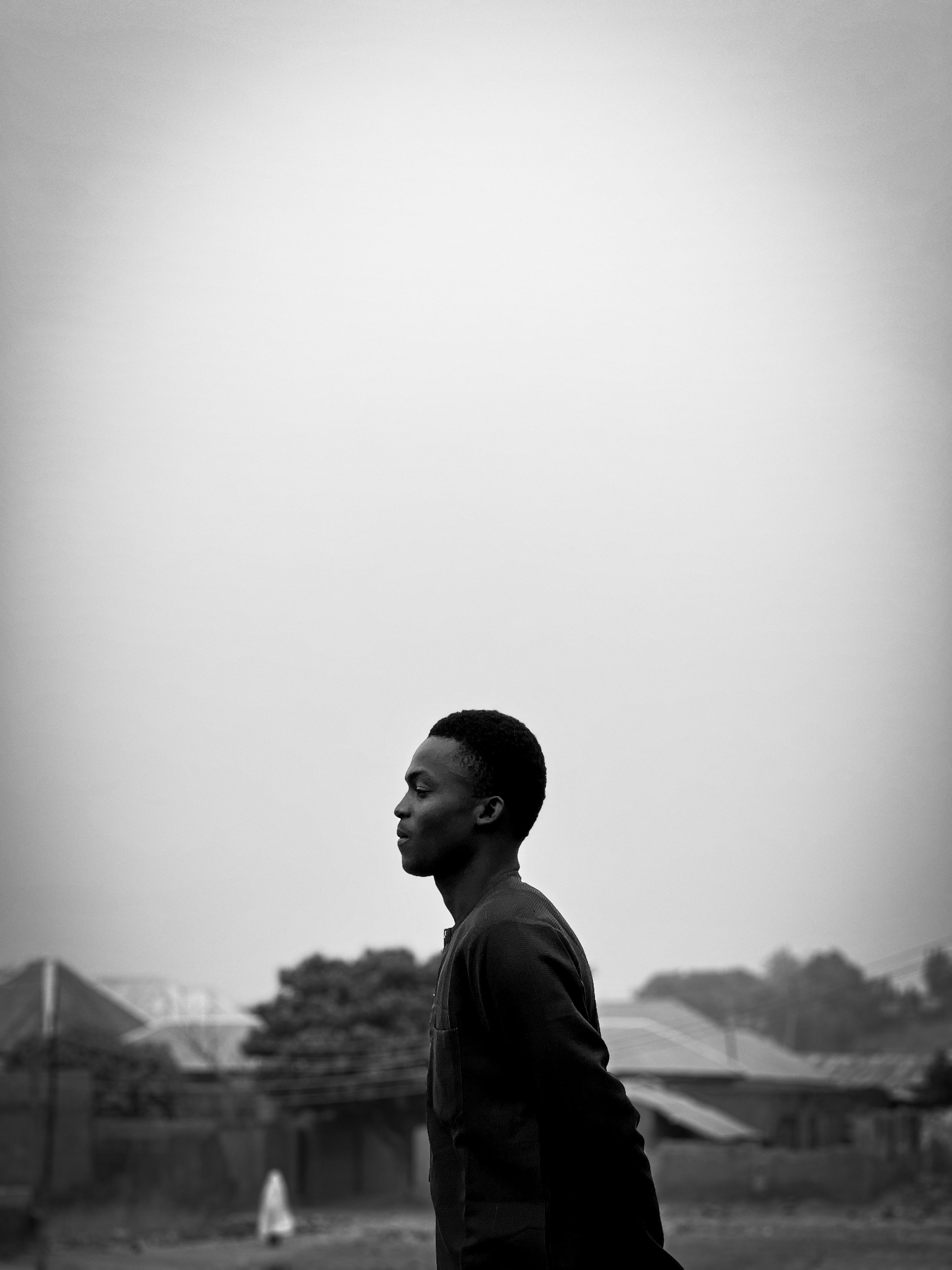 A side profile black and white photo of a young man outdoors with a serene background.