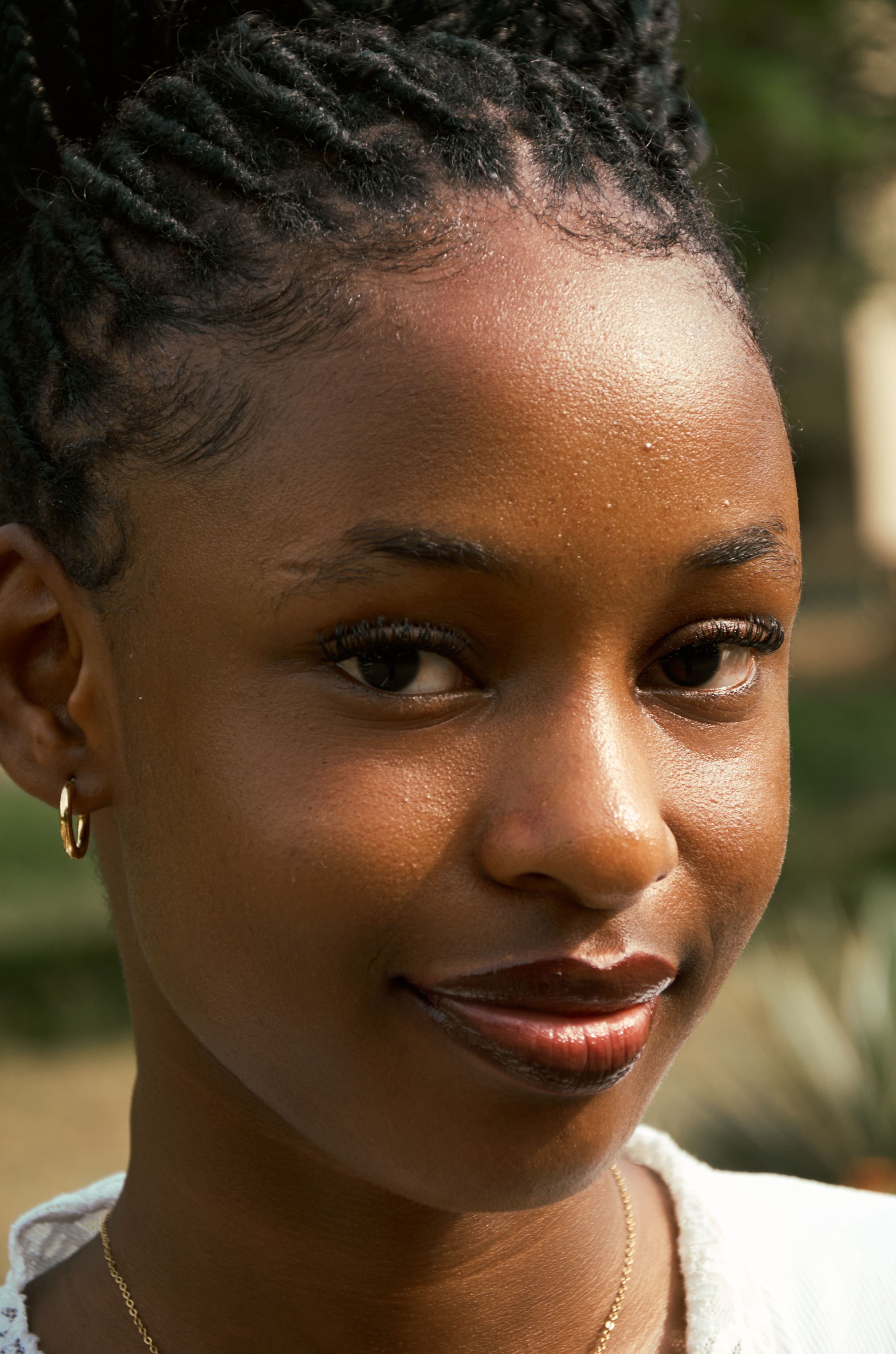 Close-up portrait of a young woman outdoors with braided hair and a serene expression.