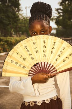 Portrait of a young woman holding an ornate traditional Asian fan outdoors. Cultural and stylish imagery.