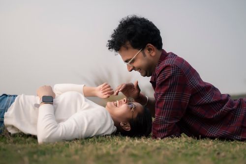 Free A joyful couple enjoys a moment of laughter while lying on grass outdoors. Stock Photo