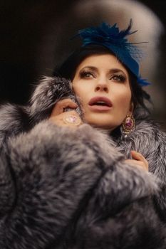 Woman in luxurious fur with blue hat and jewelry, showing elegance.