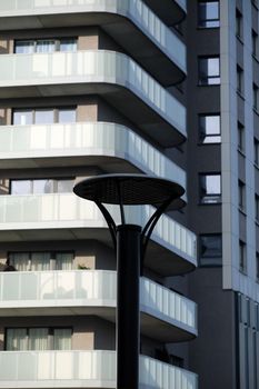 Modern apartment building with unique rounded balconies and a silhouetted street lamp in foreground.