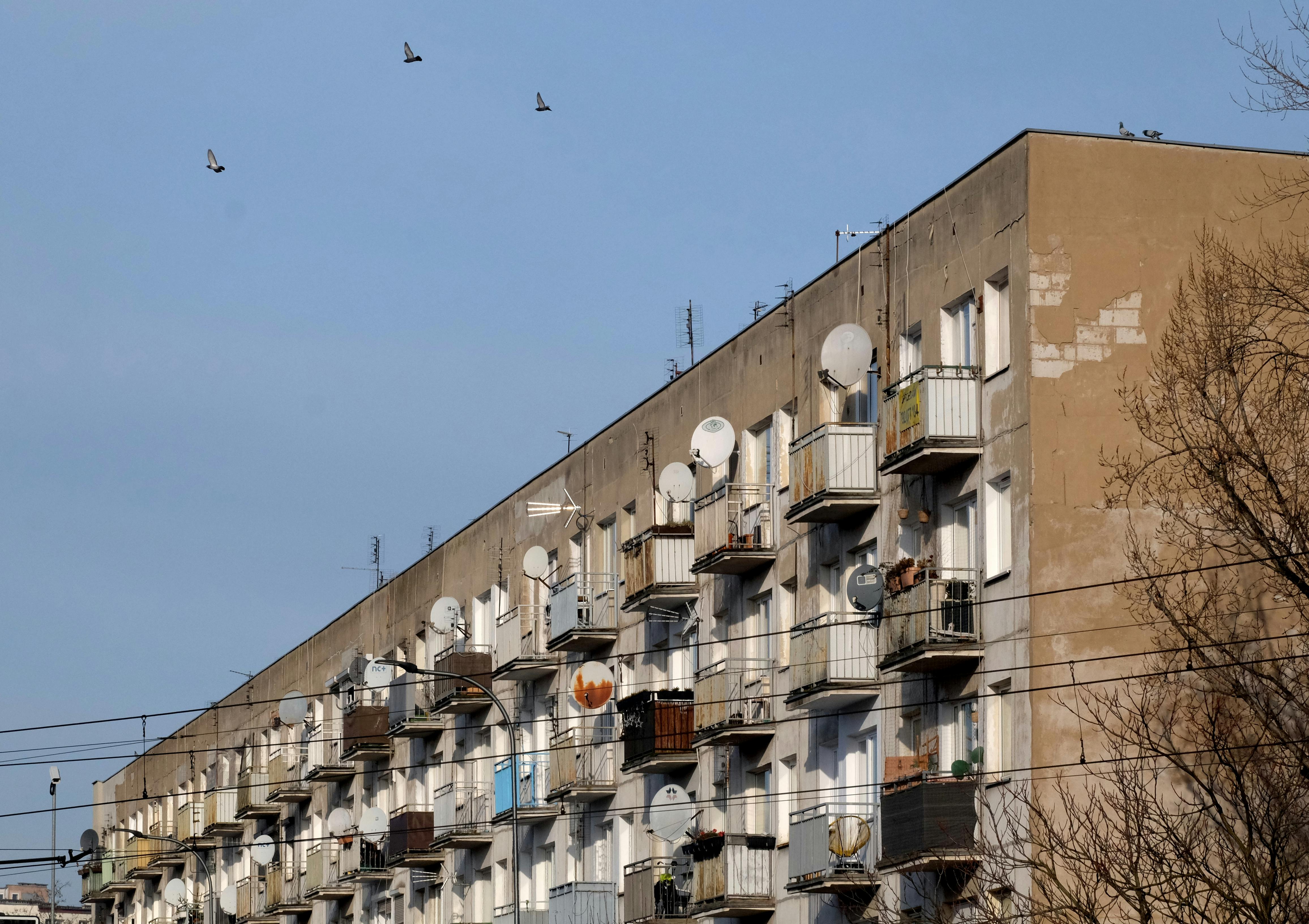 City apartment building with multiple balconies and satellite dishes under a clear sky.