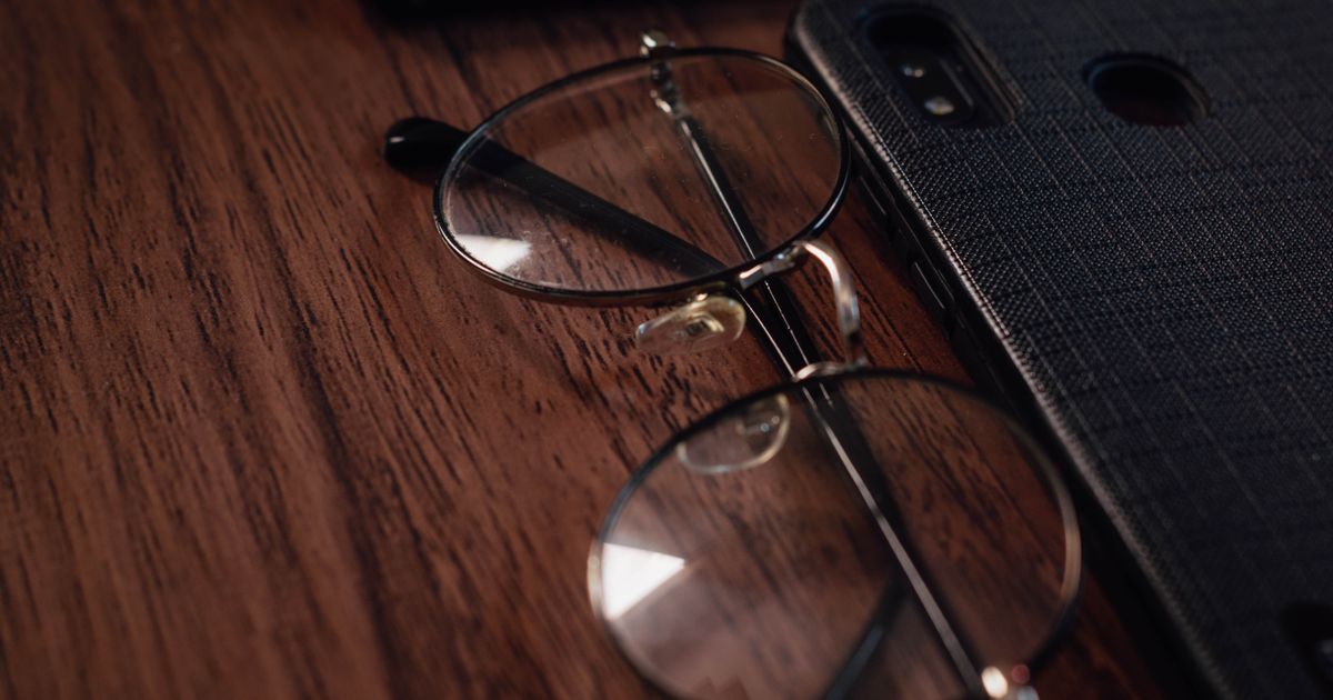 A pair of eyeglasses resting beside a smartphone on a table.