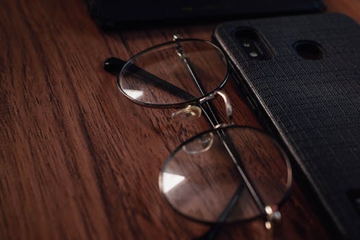 Smartphone and eyeglasses resting on a wooden table, close-up view.