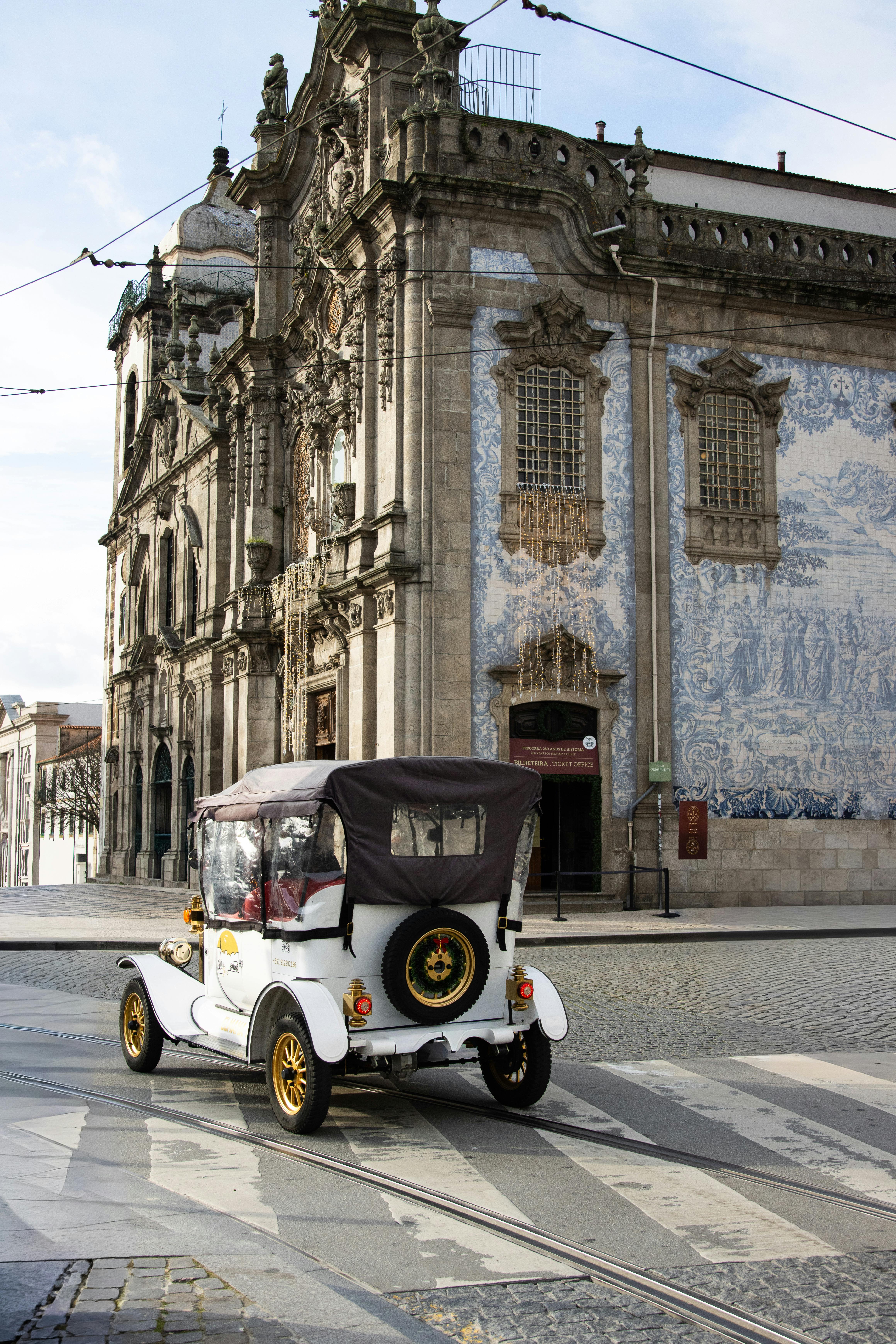 A classic car driving by a historic building with blue tiles in Porto, Portugal.