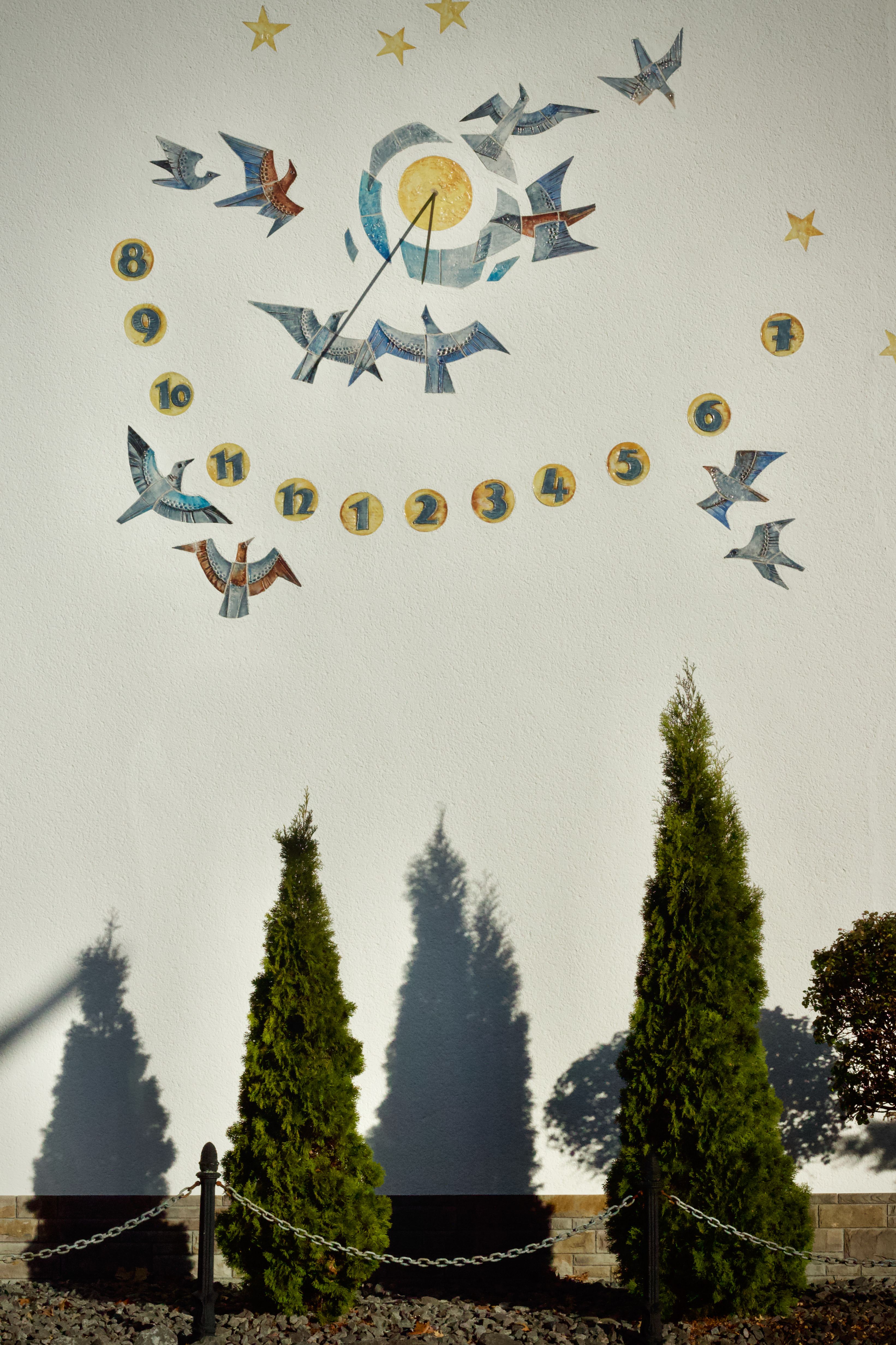 Artistic sundial with bird designs casting shadows on a sunny wall.