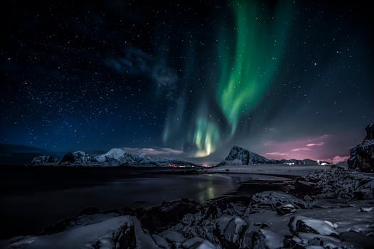 Stunning view of aurora borealis over snow-capped peaks in Nordland, Norway under a starry night sky.