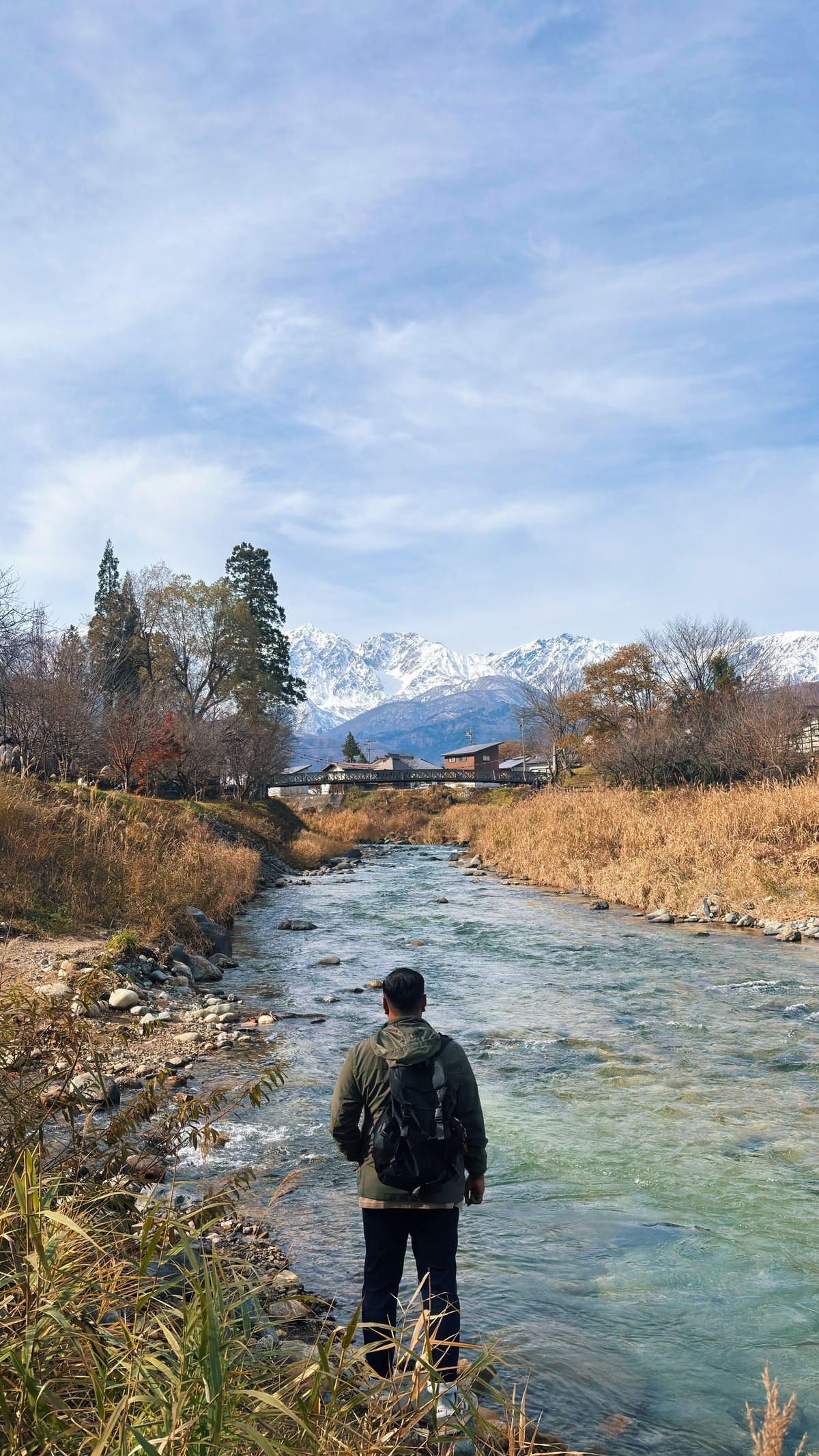 Man standing by a clear river in Hakuba, Japan during the green season