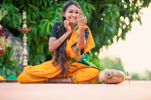 Free Smiling woman in vibrant saree poses gracefully outdoors amidst cultural decor. Stock Photo