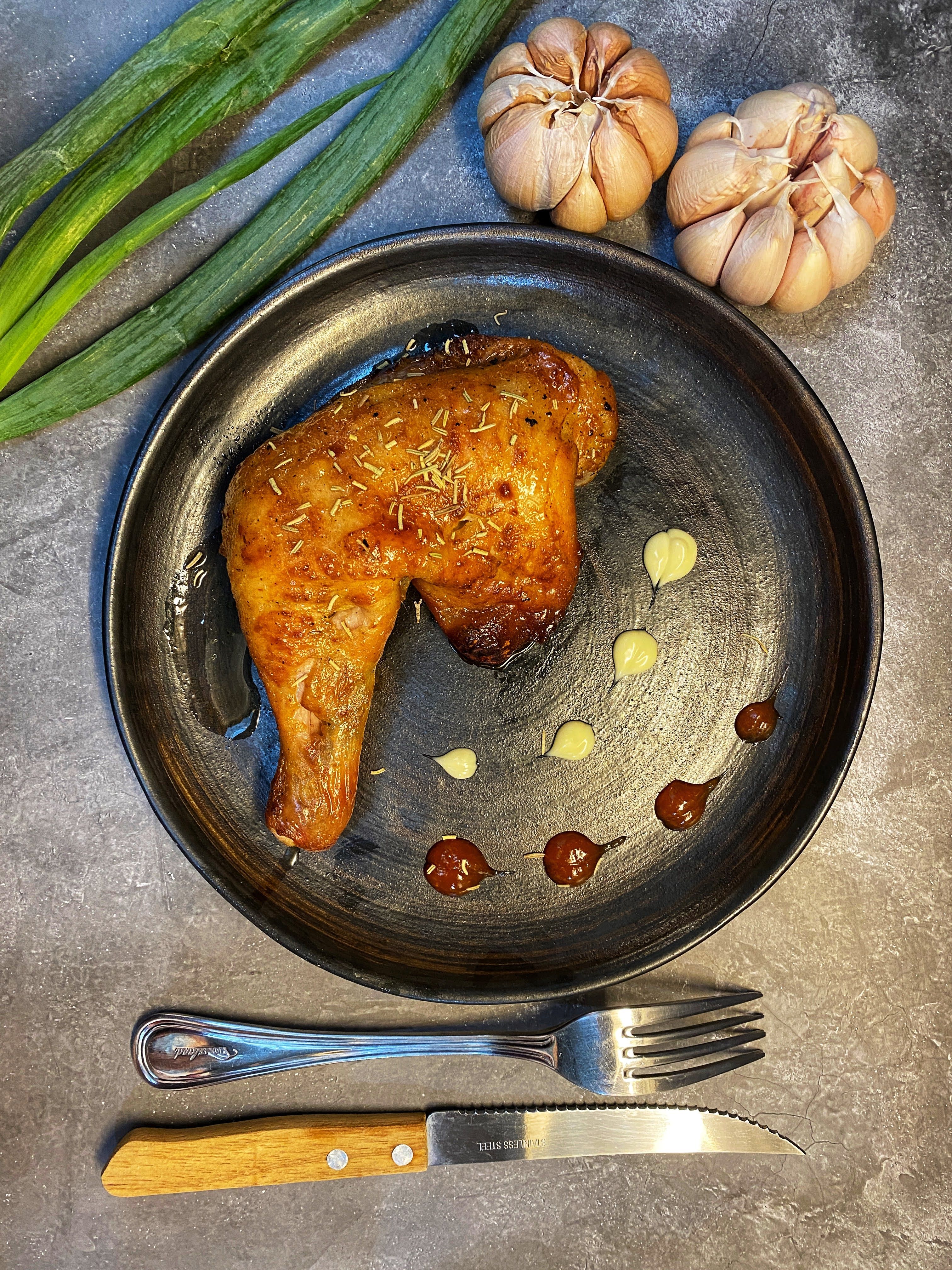 Succulent grilled chicken leg served with garlic cloves, sauce, and fresh herbs for a flavorful meal.