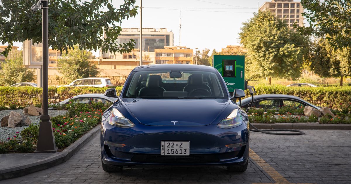 A blue Tesla Model 3 charging at an urban electric vehicle station.