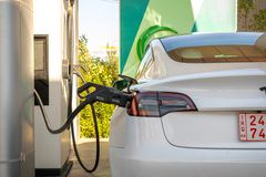 Tesla Model 3 electric vehicle charging at a station outdoors during the day.