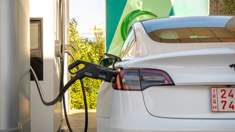 Tesla Model 3 electric vehicle charging at a station outdoors during the day.