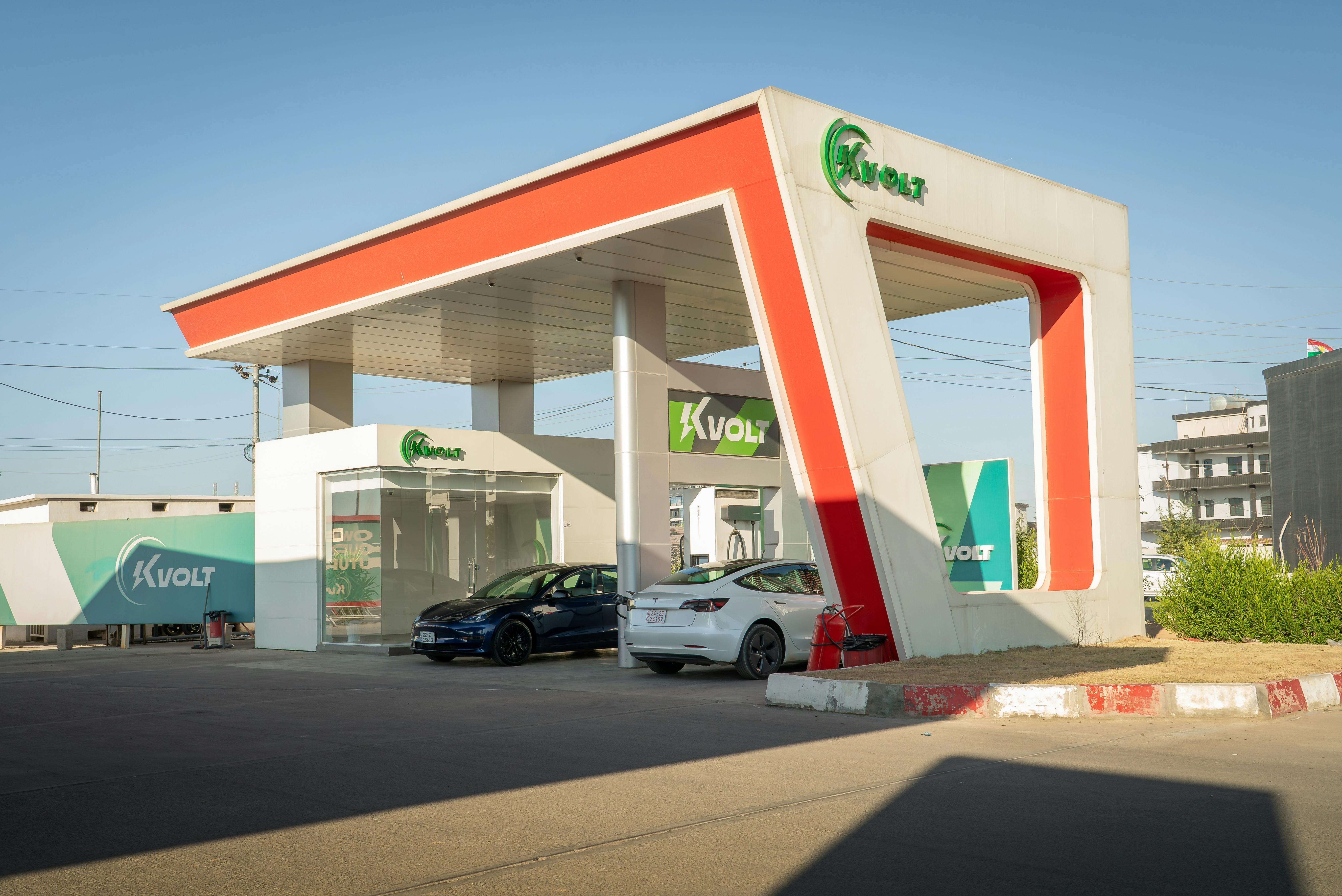 A futuristic electric vehicle charging station featuring Tesla cars under a bright blue sky.