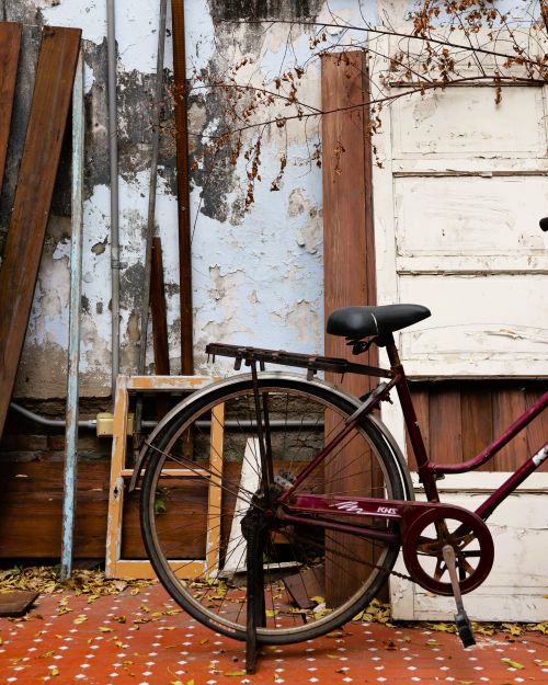 Free Rusty bicycle leaning against a rustic wall with autumn leaves on the ground in Taiwan. Stock Photo