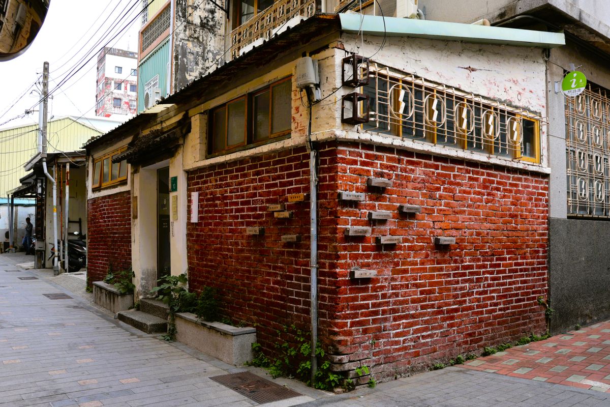 A red-brick shophouse corner, quiet in the morning light, before any stall smoke reaches it. The street smelled like nothing yet, which in this city means you're early.