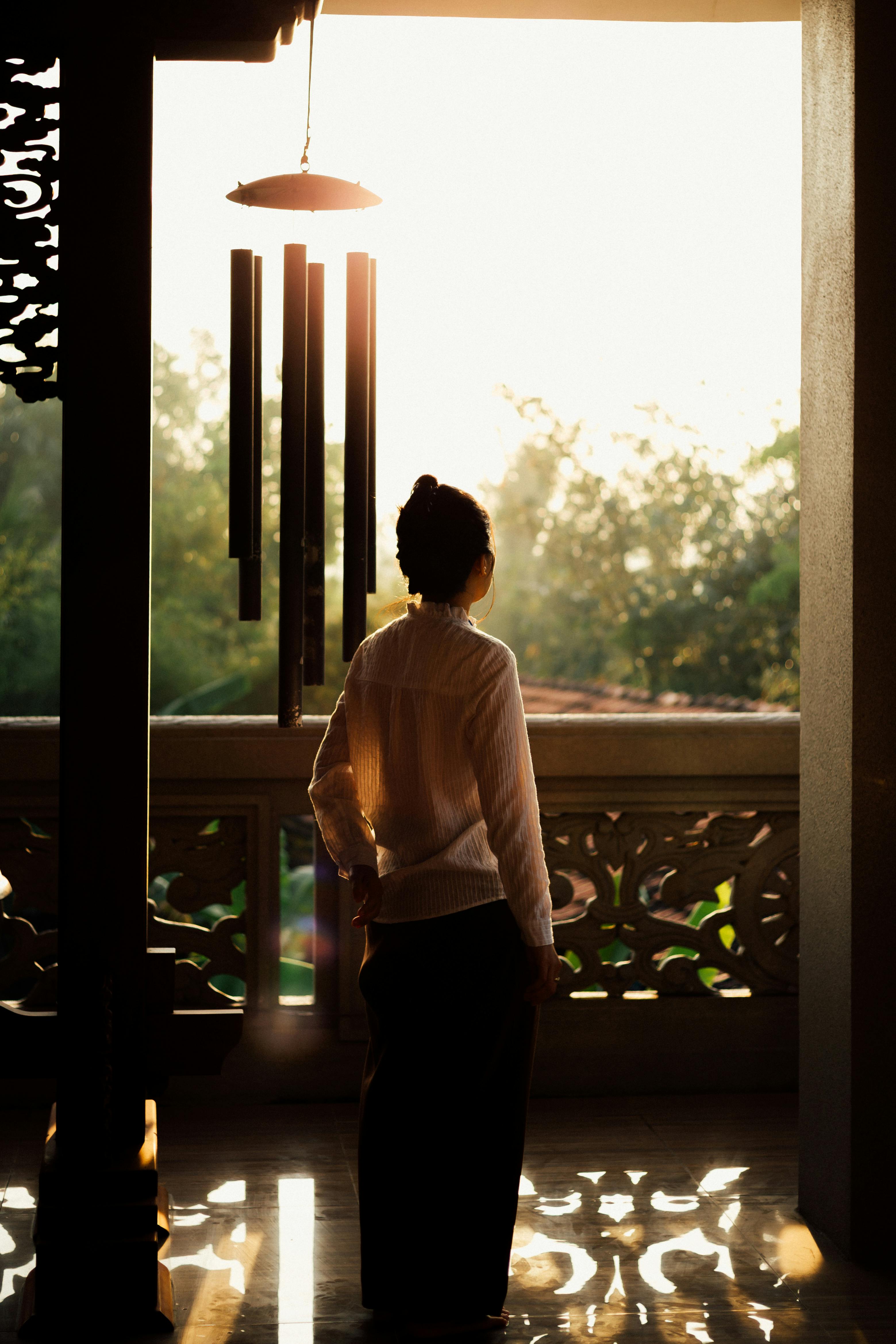 A woman gazes at sunset from a serene balcony, creating a peaceful silhouette.