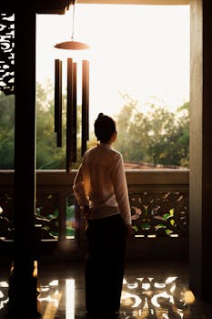 A woman gazes at sunset from a serene balcony, creating a peaceful silhouette.