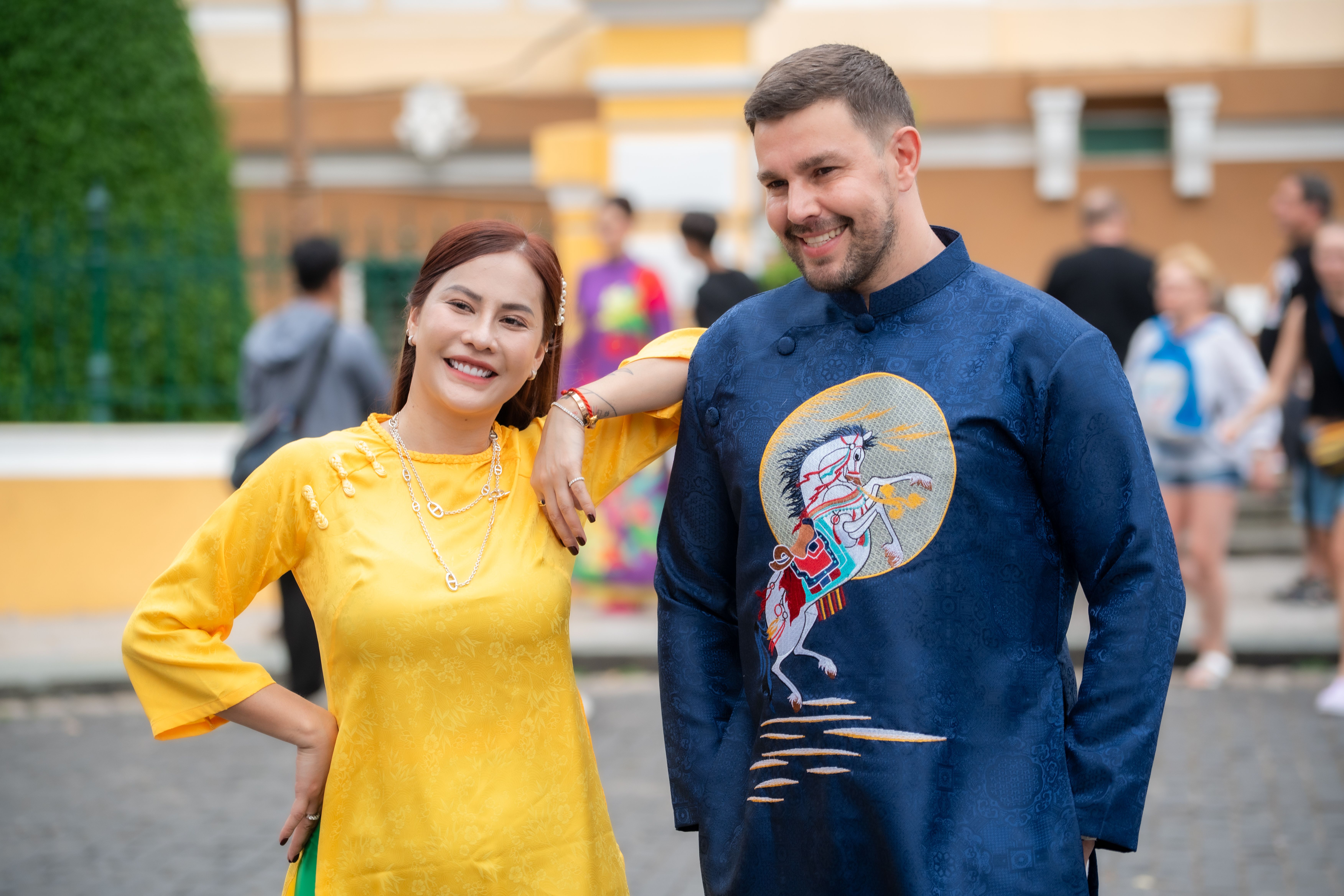 A couple in traditional Vietnamese clothing enjoys a cheerful moment outside, showcasing vibrant attire and smiles.
