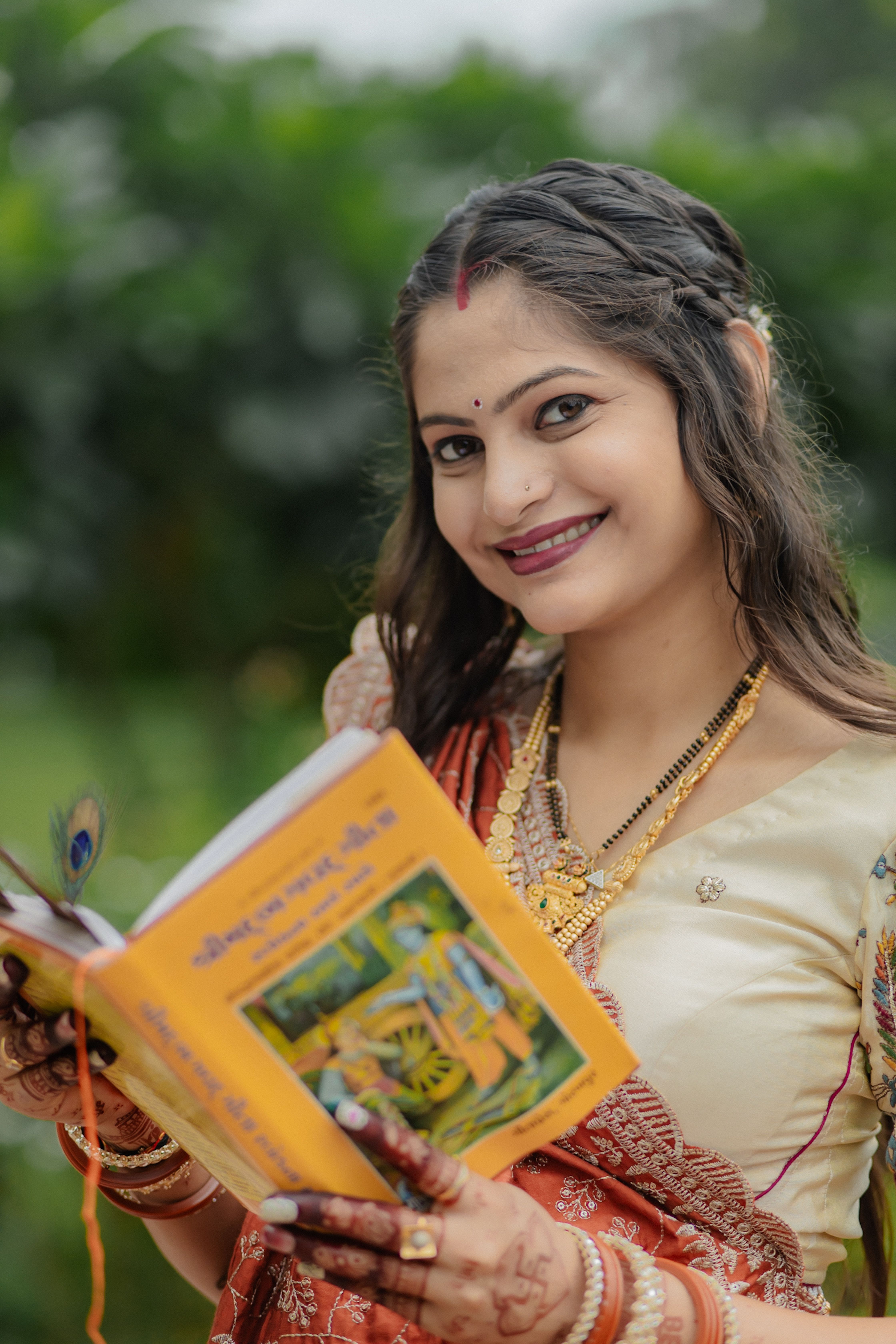 Woman in traditional attire reading a religious book outdoors with a joyful expression.
