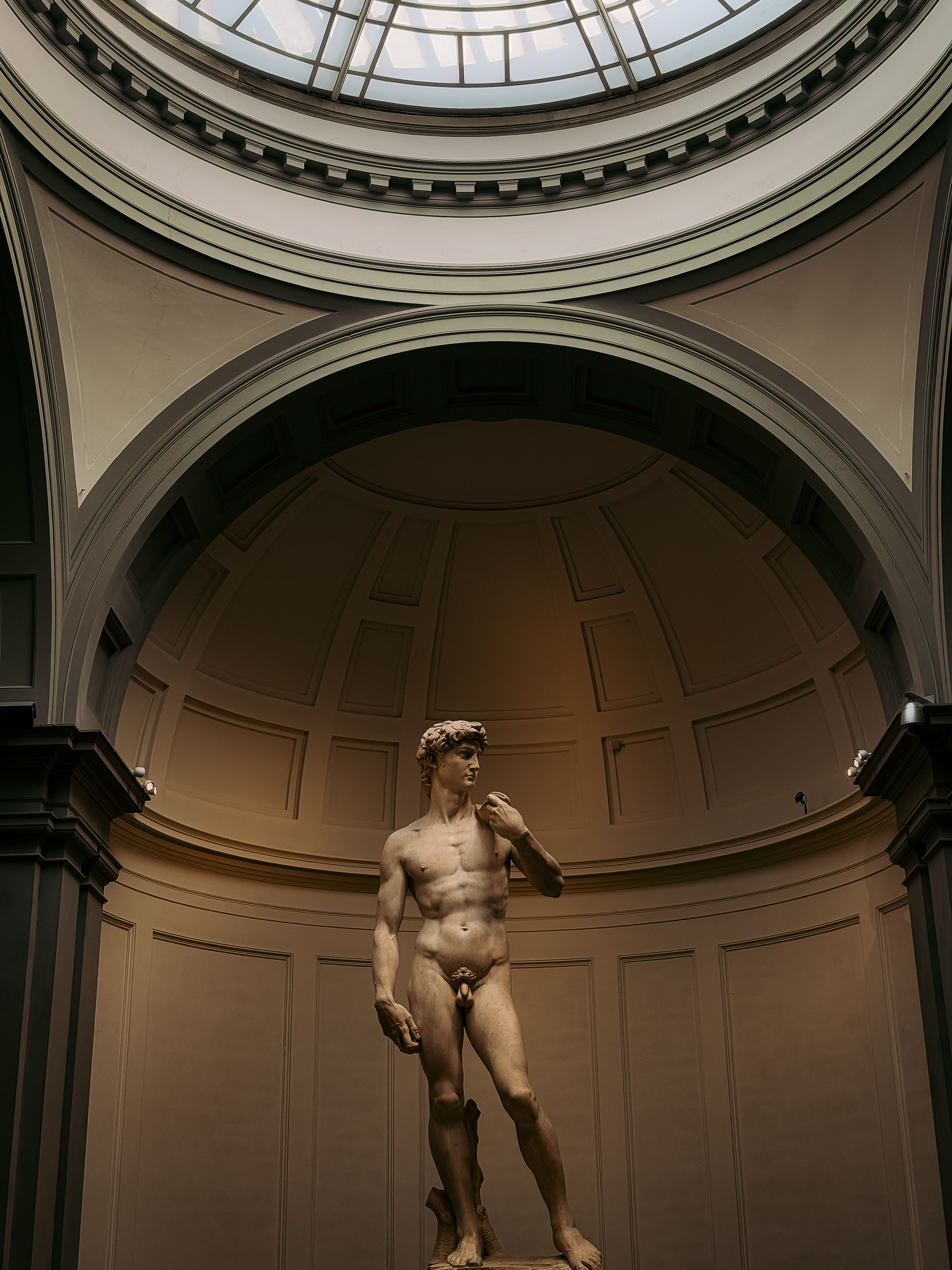 View of Michelangelo's David under a glass dome in Florence, highlighting classic Renaissance art.