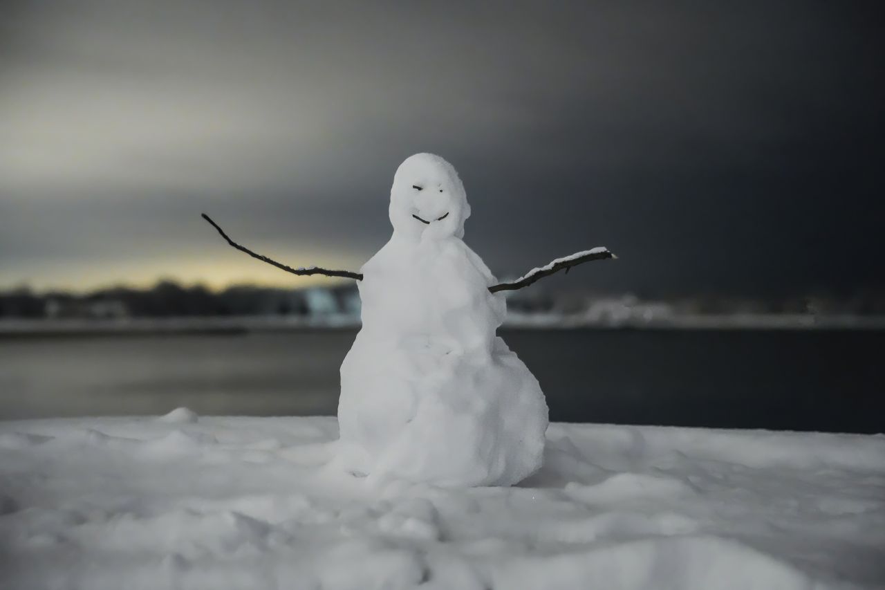 a playful snowman stands by a serene lakeside silhouetted against the